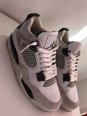 Air Jordan 4 Retro Vit/Grå - Snygga Air Jordan 4 Retro sneakers i vitt och ljusgrått med svarta detaljer. Ovandelen är i läder och mocka med meshpaneler för extra ventilation. Klassisk Jumpman-logga på plösen och stabil sula för skön komfort.