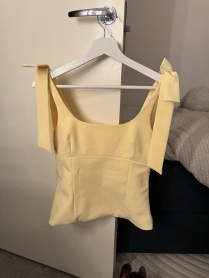 Zara gul topp med rosetter - Säljer denna gula toppen från Zara då den inte kommer till användning. Den har en liten smink fläck inuti (bild 4) men som går att tvätta bort!