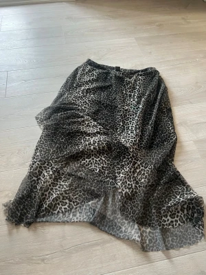 Leopardmönstrad långkjol från Lindex - Säljer en snygg långkjol från Lindex med leopardmönster i svart och beige. Kjolen har ett tunt, flygigt material och resår i midjan för skön passform. Perfekt för dig som vill sticka ut lite extra med ett djurmönstrat plagg.