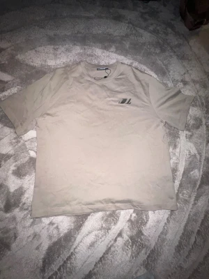 Beige t-shirt från J.Lindeberg - Säljer en stilren beige t-shirt från J.Lindeberg med diskret logga på bröstet. Klassisk passform och rund halsringning, perfekt till jeans eller shorts. Tillverkad i mjuk bomull för skön känsla hela dagen.