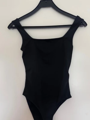 Svart body  - En stilren svart body med breda axelband och rak urringning. Enkel och tidlös design . Tillverkad i stretchigt material för bekväm passform.