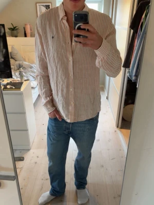 Morris linneskjorta  - Säljer en snygg randig skjorta från Morris i ljusorange och vitt. Skjortan är tillverkad i linne, har lång ärm, klassisk krage och knappar framtill. Skjortan är använd ett fåtal gånger och är i inprincip i ny skick. Denna linneskjorta är perfekt nu till sommaren då den är lite luftigare. Modellen är 181 cm, lite förstor på han! Pris går att diskuteras vid en snabb affär! Vid frågor är de bara att höra av sig!