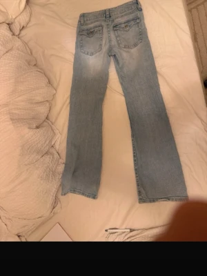 Ljusblå raka jeans med slitningar lågmidjadd - Säljer ett par ljusblå jeans med raka ben och klassisk femficksmodell. jeansen är lågmidjade Jeansen har subtila slitningar framtill och bakfickor med enkel söm. Perfekta för en avslappnad och trendig look. Materialet är denim i bomull.
