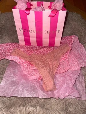 Spetsstring i rosa från Victoria's Secret - Säljer en snygg rosa stringtrosa från Victoria's Secret. Trosan är i spetsmaterial med fina detaljer och har en feminin, låg midja. Perfekt för dig som gillar både komfort och stil. Kommer i originalförpackning med presentpåse.