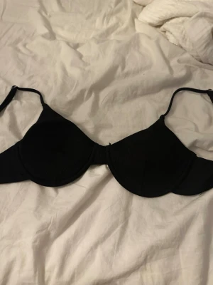 Svart bygel-bh med justerbara band - Snygg svart bikiniöverdel med bygel och justerbara axelband. Klassisk och stilren modell som passar perfekt till stranden eller poolen. Enkel design utan mönster och med lätt vaddering för extra stöd.