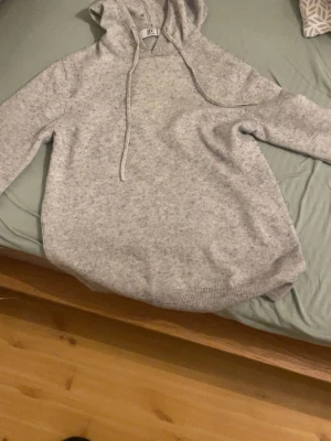 Ljusgrå kashmir hoodie från BVALDI. 1300 nya  - Mysig ljusgrå hoodie från BVALDI med huva och dragsnören. Tillverkad i mjukt material som känns skönt mot huden. Perfekt för chill dagar och enkel att matcha med jeans eller mjukisbyxor. Klassisk passform och ribbade muddar vid ärmslut och nederkant.