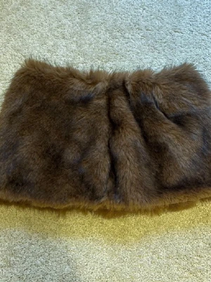 Brun pälsimitation kortkjol - Säljer en fluffig brun kortkjol i pälsimitation med dragkedja i sidan. Kjolen har en mjuk och lyxig känsla, perfekt för dig som vill sticka ut med en unik look. Passar till många olika stilar och är superenkel att matcha.