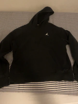 Svart hoodie från Jordan - Säljer en svart hoodie från Jordan med den klassiska Jumpman-loggan broderad i vitt på bröstet. Hoodien har en rymlig huva och är tillverkad i mjukt material, perfekt för en avslappnad och sportig stil.