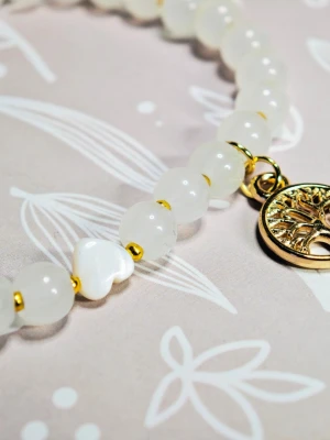 Vitt pärlarmband med livets träd-berlock - Stilrent armband med vita runda glaspärlor och guldfärgade detaljer. Armbandet har en söt hjärtformad pärla i pärlemor och en guldfärgad berlock med livets träd. Perfekt accessoar för dig som gillar enkla men snygga smycken. Stretchigt armband, 18 cm i omkrets.