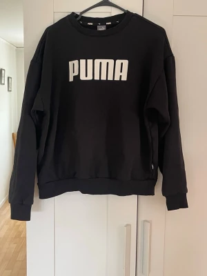 Svart sweatshirt från Puma - Snygg svart sweatshirt från Puma med stort vitt logotryck på bröstet. Tröjan har rund halsringning, långa ärmar och ribbade muddar vid ärmslut och nederkant. Tillverkad i mjukt och bekvämt material, perfekt för en avslappnad stil. Tveka inte på att höra av dig om du har några frågor!💕 svarar snabbt