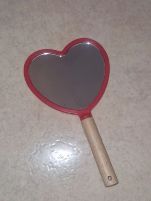 Spegel - Söt liten spegel formad som ett hjärta med röd ram och praktiskt handtag i ljust trä. Perfekt storlek för att hålla i handen när du sminkar dig eller fixar håret etc. Inga defekter