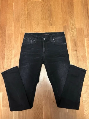 Svart/gråa slim fit jeans från Nudie Jeans - Snygga svarta slim fit jeans från Nudie Jeans med klassisk femficksmodell och diskreta kontrastsömmar. Jeansen har normal midja och raka ben, tillverkade i mjuk denim med lite stretch för extra komfort. W27 L30 hör av er vid frågor eller funderingar🙌✅