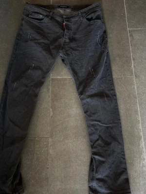 Grå jeans från Dsquared2 - Säljer ett par grå jeans från Dsquared2 med smal passform och slitna detaljer. Jeansen har klassisk femficksmodell, bälteshällor och knappgylf. Materialet är bomull med en mjuk känsla och stretch för extra komfort.