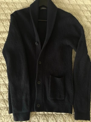 Mörkblå stickad cardigan - Säljer en mörkblå stickad cardigan från dressmann i storlek S, sjukt snygg och stilren och även perfekt till en simpel outfit. Hör av er vid ytterligare frågor! Mvh