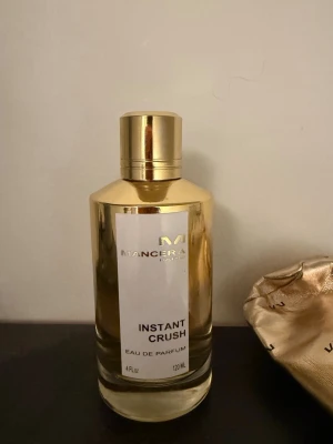 Mancera Instant Crush Eau de Parfum - Lyxig parfym från Mancera, Instant Crush, i en elegant guld- och glasflaska med metallock och svart blomdetalj på toppen. Flaskan rymmer 120 ml och har en modern, stilren design som verkligen sticker ut på parfymhyllan. Parfymen är bara testad 