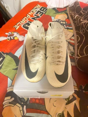 Nike Zoom Mercurial vita fotbollsskor - Säljer ett par vita Nike Zoom Mercurial fotbollsskor med högt skaft och svarta detaljer. Skorna har snörning, en stor svart Nike-swoosh på ovansidan och texten 'Zoom' på sidan. Tillverkade i syntetmaterial för bra grepp och lätt känsla på planen.