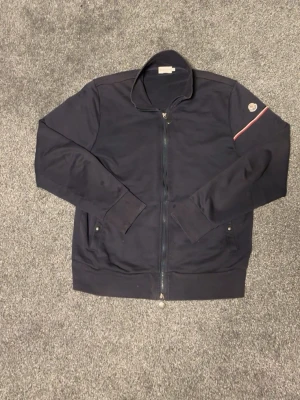 Moncler Zip Up - Säljer en självklart äkta Moncler Zip up! Passar storlek S, har en liten reva på inner-armen mrn annars är den i övrigt gott skick. Tveka inte att höra av dig vid minsta lilla fråga!