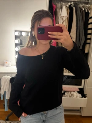 Svart stickad tröja - En svart off shoulder tröja med lång ärm och avslappnad passform. Tröjan har en enkel design utan synliga loggor eller mönster och är perfekt att styla med jeans. Materialet ser mjukt och bekvämt ut.