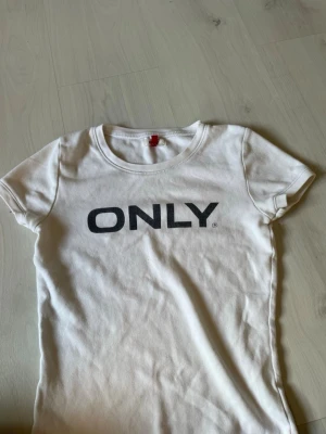 Vit t-shirt från ONLY med tryck - Säljer en vit t-shirt från ONLY med svart tryck på bröstet. Klassisk rund halsringning och korta ärmar. Tillverkad i mjuk bomull för en bekväm känsla. Perfekt till jeans eller shorts för en enkel och clean look.