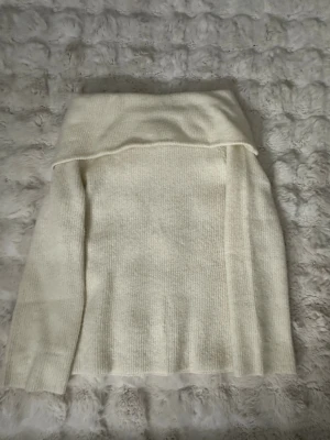 Offshoulder stickad tröja cremevit - Säljer en cremevit stickad tröja med offshoulder-krage. Tröjan har lång ärm och är ribbstickad i mjukt material. Perfekt för dig som gillar en stilren och trendig look.