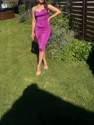 Lila tight klänning med smala axelband, XS - Säljer en snygg lila klänning med smala axelband och figurnära passform. Klänningen är knälång och har en lätt glansig yta som ger en lyxig känsla. Perfekt för dig som vill sticka ut! Materialet känns som polyester.