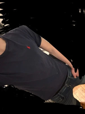 Mörkblå t-shirt från Ralph Lauren - Klassisk mörkblå t-shirt från Ralph Lauren med den ikoniska röda broderade loggan på bröstet. T-shirten har rund halsringning och korta ärmar, perfekt för en clean och stilren look. Tillverkad i mjuk bomull för skön komfort.