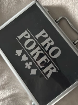 Pro Poker pokerset i aluminiumväska - Säljer ett komplett pokerset från Pro Poker i en snygg aluminiumväska. Innehåller marker i blått, grönt, svart och rött, två kortlekar, tärningar och en dealer-bricka. Perfekt för pokerkvällar med vänner. Väskan är svart med silverdetaljer och har ett robust handtag.