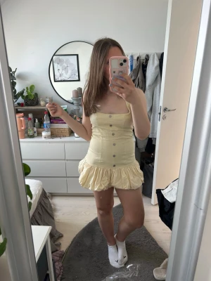 Ljusgul kort klänning - Peppermayo - Söt ljusgul kort klänning med knappar framtill och volang nedtill. Klänningen har halterneck och även stretch baktill som ger den en bättre passform💕 