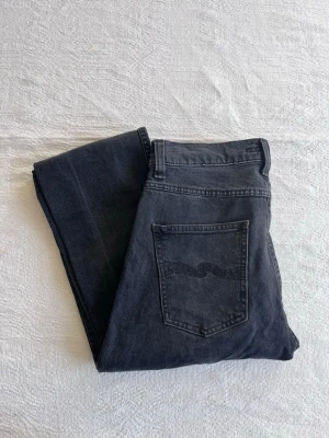 Nudie Jeans Grim Tim Dark Cove, w29 L32, fint skick - Säljer ett par svarta jeans från Nudie Jeans med klassisk femficksmodell och rak passform. Modell Hrim Tim. Jeansen har en diskret logga på bakfickan och är tillverkade i mjuk denim. Perfekta för en clean och stilren look.