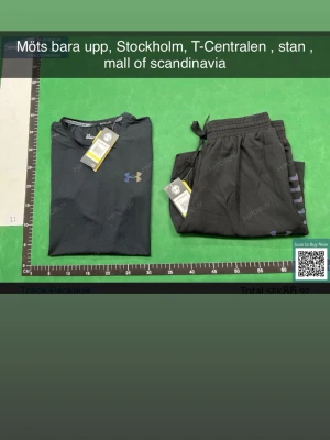 Svart träningsset från Under Armour - Säljer ett svart träningsset från Under Armour med t-shirt och shorts. T-shirten har en diskret logga på bröstet och är tillverkad i ett lätt, snabbtorkande material. Shortsen har dragsko i midjan och matchande design, perfekta för löpning eller gym.