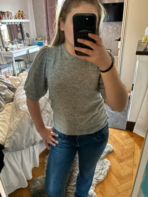Grå topp med puffärm - Snygg grå topp med puffärmar och rund halsringning. T-shirten har en enkel och stilren design som passar perfekt till jeans eller kjol. Mjuk och bekväm, perfekt för dig som gillar en clean look.