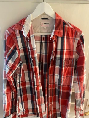 Rutig skjorta från Knowledge Cotton - Snygg rutig skjorta i rött, vitt och blått från Knowledge Cotton Apparel. Skjortan har klassisk krage, knappar framtill och är i slim fit-modell. Perfekt för dig som gillar en stilren och färgglad look.