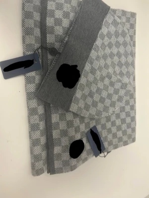 Grå rutmönstrad mössa och halsduk - Säljer en grå mössa och halsduk med stilrent rutmönster och bred ribbad kant. Mössan är tillverkad i mjukt stickat material som känns skönt mot huden. Perfekt för dig som vill ha en enkel men snygg accessoar till hösten och vintern.