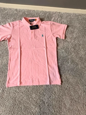 Rosa Ralph lauren piké Ny-oanvänd (S) - Säljer en helt ny och oanvänd Ralph Lauren piké i storlek S. Klassisk och stilren piké i en snygg rosa färg med den ikoniska broderade Ralph Lauren-loggan på bröstet. Tillverkad i hög kvalitet med bekvämt och luftigt material som passar perfekt för både vardag och mer uppklädda tillfällen. 🔹 Märke: Ralph Lauren 🔹 Modell: Piké 🔹 Färg: Rosa 🔹 Storlek: S 🔹 Skick: Helt ny / oanvänd 🔹 Passform: Klassisk Nypris är högt – perfekt möjlighet att göra ett fynd. Hör gärna av dig vid frågor