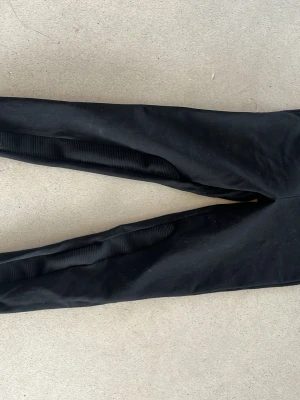 Svarta leggings från Friends - Svarta leggings från Friends med ribbade detaljer längs benen och två dekorativa dragkedjor framtill. Mjukt och stretchigt material som sitter skönt. Perfekta för en cool och avslappnad stil.