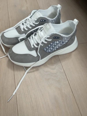 Grå och vita Zara sneakers - Snygga sneakers från Zara i grått  och vitt med klassiskt Zara-mönster på sidan. Skorna har vita snören, meshdetaljer och mockaliknande partier. Tjock vit sula ger en modern vibe och extra komfort. Perfekta för dig som gillar exklusiva och trendiga sneakers.