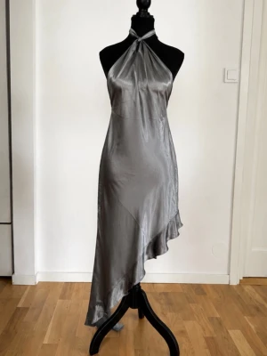 Silverfärgad halterneckklänning i satin - Superfin mörkgrå satin klänning från AsYou med halterneck/knytdetalj och asymmetrisk volangkant. Väldigt elegant och trendig modell med fin glans i tyget som faller superfint på kroppen. Perfekt till fest, middag, födelsedag eller utekväll 