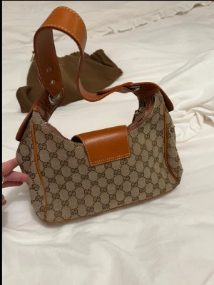 Handväska - Beige handväska med bruna läderdetaljer och bred axelrem. Väskan har silverfärgade metalldetaljer och stängs med magnetlås. Väldigt fint skick!💞