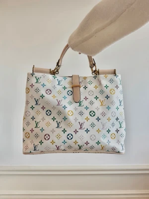 Louis Vuitton multicolor handväska - Säljer en vit handväska från Louis Vuitton med det ikoniska multicolor-mönstret i flera färger. Väskan har två handtag i ljust läder och guldfärgade metalldetaljer. Klassisk fyrkantig form och stängs med ett läderband. 