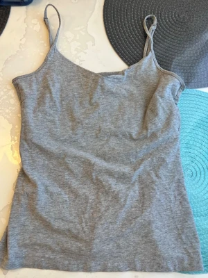 Grå enkel linnetopp - Snygg grå linnetopp med smala axelband och enkel design. Perfekt att matcha med jeans eller kjol för en avslappnad look. Tillverkad i mjukt bomullsmaterial som känns skönt mot huden.