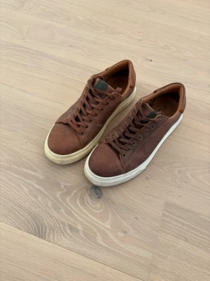 Bruna sneakers i läder - Snygga bruna sneakers från playboy i läder med klassisk låg profil och vit, chunky sula. Skorna har bruna skosnören och diskret logga på plösen. Perfekta för en stilren och avslappnad look. Som ni ser så är den ena sulan vitare än den andra 