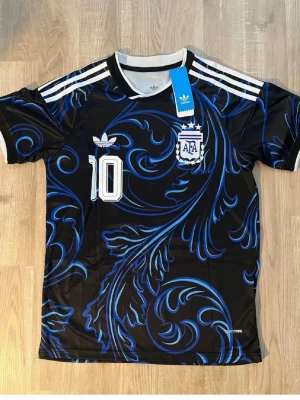 Argentinas vm tröja Messi S - Snygg svart Argentina fotbollströja från Adidas med blått mönster, vita detaljer och nummer 10. Messi står på ryggen. Tröjan har korta ärmar, rund hals och är tillverkad i ett lätt, andningsbart material. Perfekt för dig som älskar fotboll och vill sticka ut på planen.