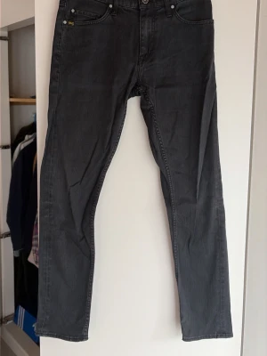 Svarta jeans från Tiger of Sweden - Säljer ett par svarta jeans från Tiger of Sweden med klassisk femficksmodell och raka ben. Jeansen har diskret logga på bakfickan och patch i läder bak i midjan. Snygg tvätt och passar perfekt till en trendig streetwear-look.