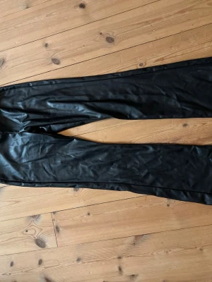 Svarta leggings i fuskskinn - Säljer ett par svarta leggings i glansigt fuskskinn. De har en tight passform och hög midja som ger en snygg siluett. Perfekta att styla med oversized tröja eller crop top för en trendig look.