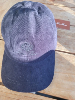 Mörkblå Loro Piana Keps - Snygg mörkblå keps från Loro Piana. Kepsen har broderad logga framtill och justerbar rem bak. Insidan har rutigt foder som ger en extra stilren touch. Perfekt accessoar för en trendig och avslappnad look.