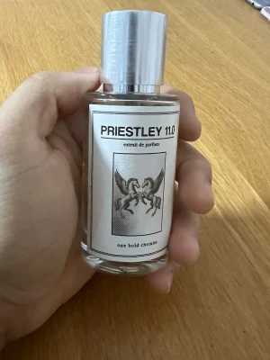 Priestley 11.0 Extrait de Parfum - Säljer en stilren parfymflaska från Priestley med namnet 11.0. Flaskan är genomskinlig med en silverfärgad metallkork och har en etikett med två bevingade hästar. Parfymen har en modern och minimalistisk design, perfekt för dig som gillar unika dofter.