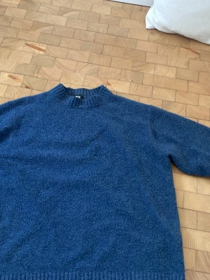 Blå stickad tröja med rund hals - Mysig blå stickad tröja från unqilo med rund hals och ribbade muddar vid ärmslut och nederkant. Perfekt för kyliga dagar men även sommarkvällar och enkel att matcha med jeans.  Tröjan har en klassisk passform och är tillverkad i ett mjukt, värmande material.