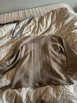 Beige stickad tröja med vågmönster - Säljer en beige stickad tröja med lång ärm och ett snyggt vågmönster längs hela ryggen. Tröjan har en rak passform och är tillverkad i ett mjukt, tunt garn som känns skönt mot huden. Perfekt för dig som gillar stilrena och enkla plagg med en twist.