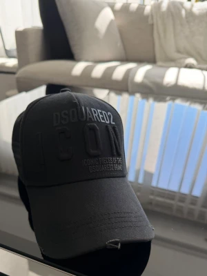 Svart keps från Dsquared2 ICON - Snygg svart keps från Dsquared2 med broderad text 'ICON' framtill och justerbar rem baktill. Kepsen är tillverkad i bomull och har en klassisk böjd skärm. Perfekt för att lyfta din streetwear-look.