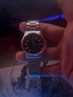 Klassisk silverfärgad Casio klocka - Stilren Casio armbandsklocka i rostfritt stål med svart urtavla och datumvisning. Klockan har en klassisk rund form och länkat armband som ger en tidlös look. Perfekt accessoar för dig som gillar enkel och snygg design.